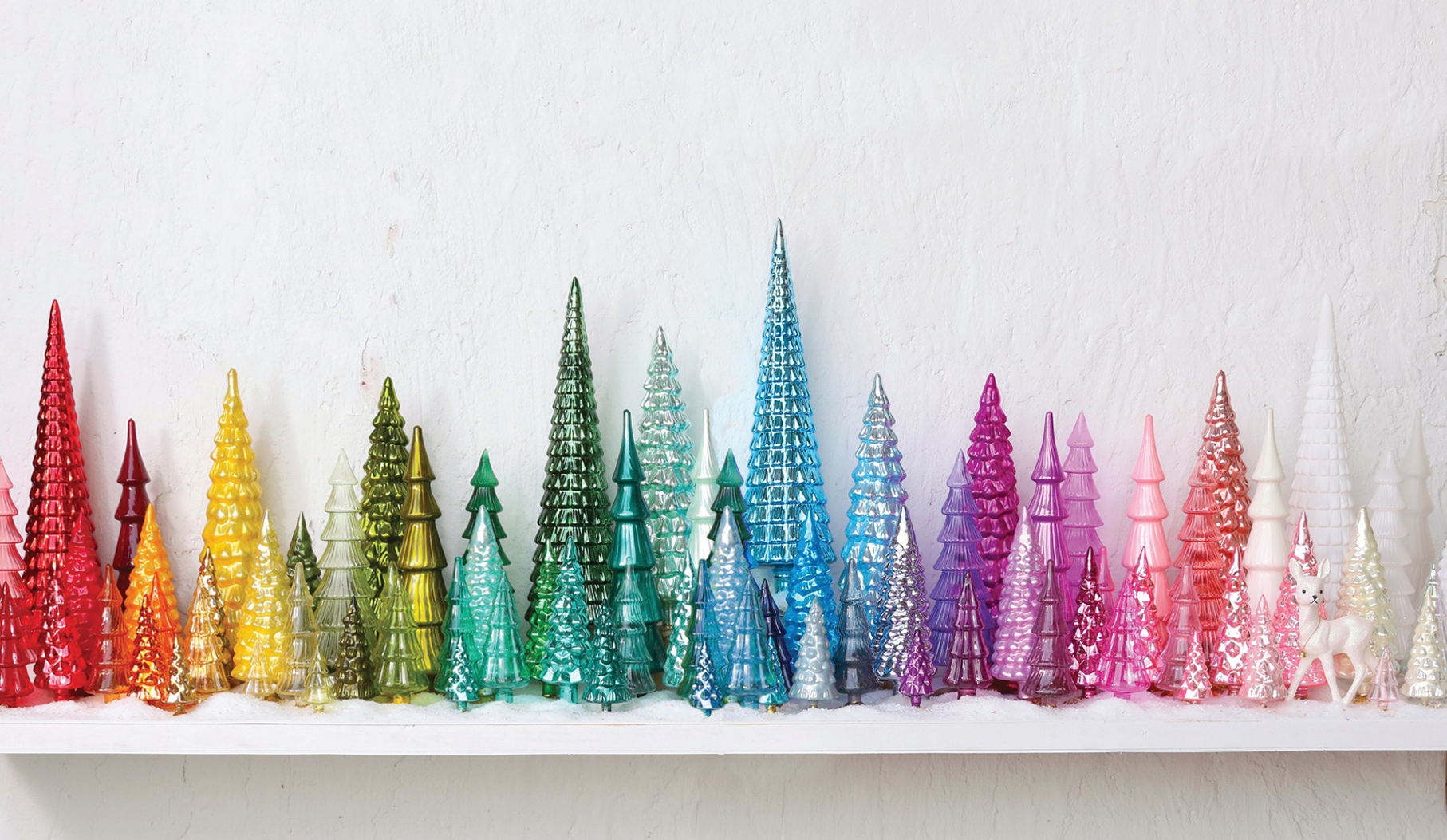 Colorful glass Christmas trees on a white shelf against a white wall