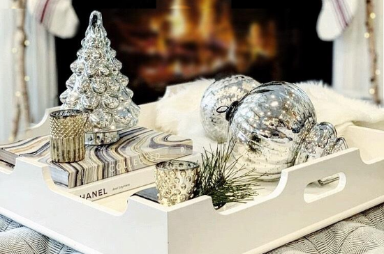 Decorative tray with Christmas ornaments including a tree, balls, and a candle on a blurred background.